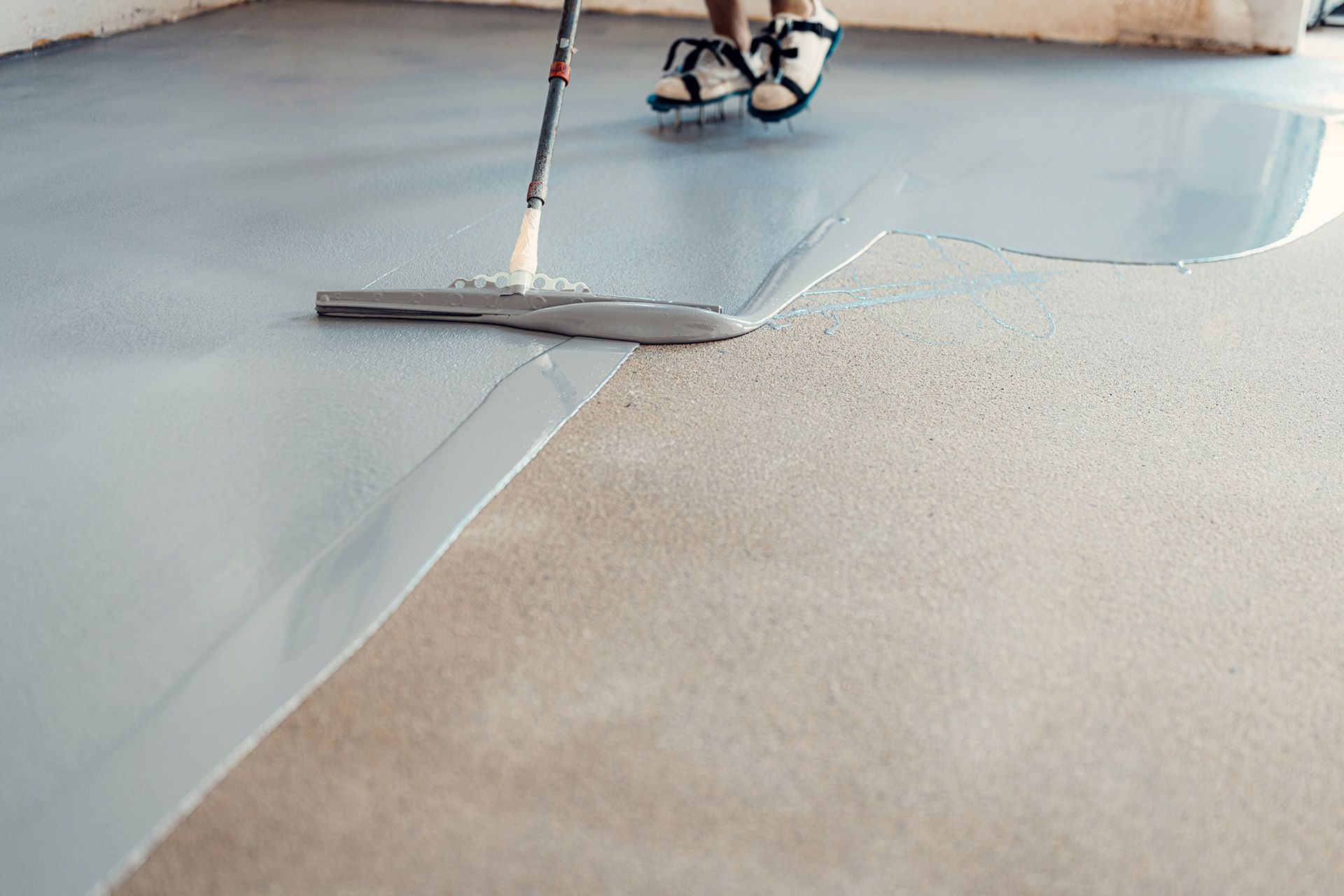 Person smoothing gray flooring with a squeegee in a room under construction