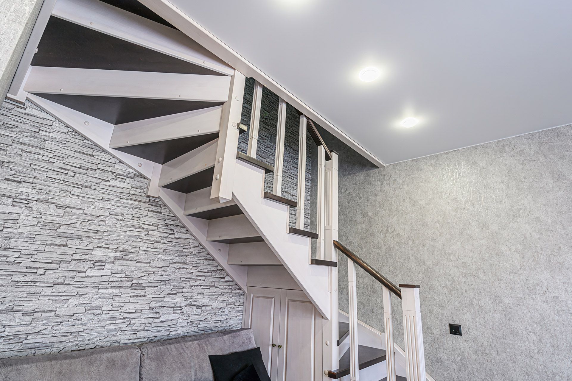 Modern indoor staircase with white steps, wood railings, stone accent wall, and recessed ceiling lights