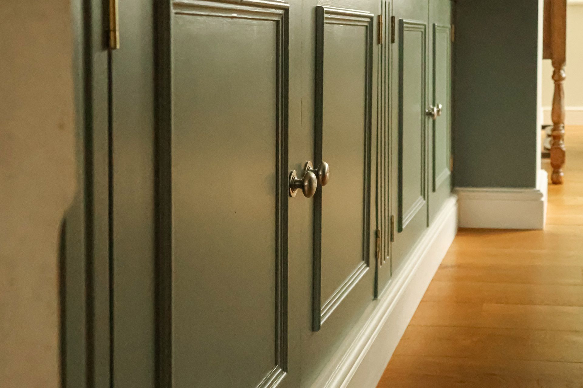 Gray paneled cabinets with silver knobs along a hallway next to a hardwood floor