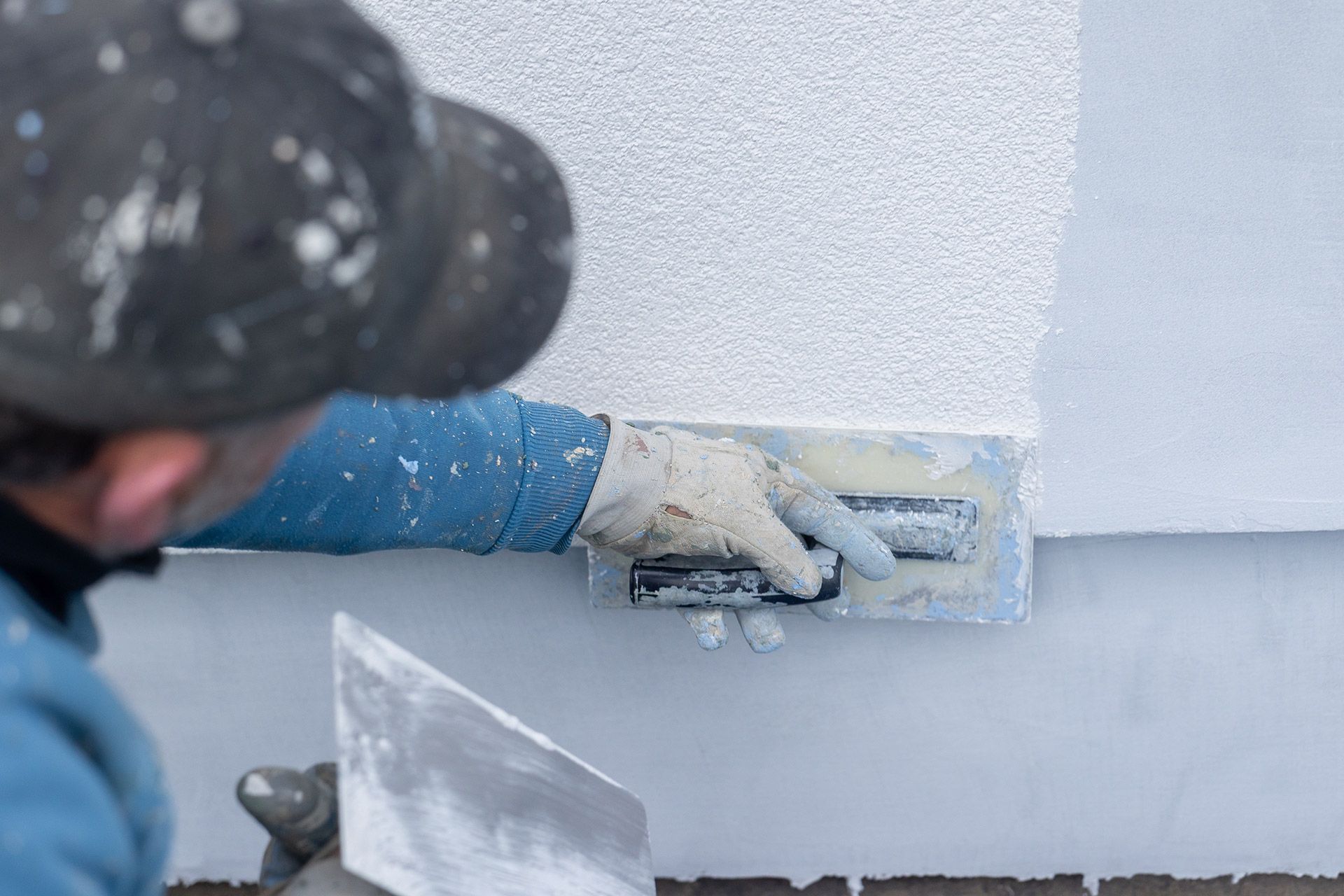 Worker applying plaster to a white wall with a trowel during interior finishing work