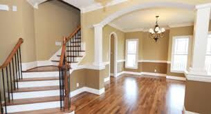 Spacious empty living room with hardwood floors, beige walls, white columns, and a staircase.