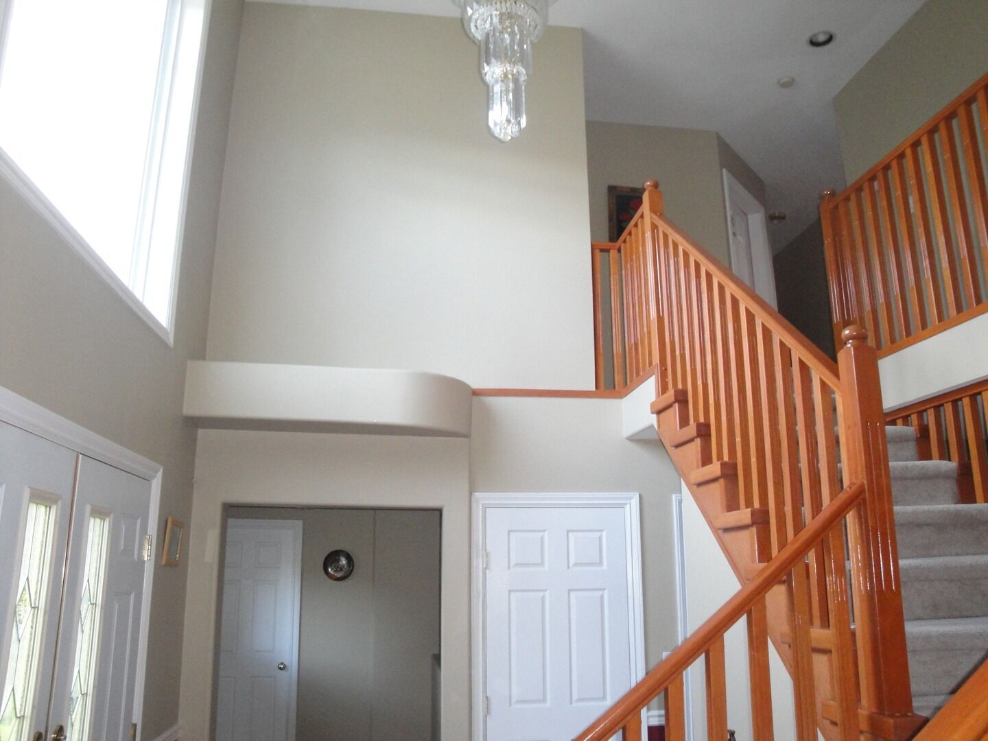 Bright foyer with staircase, white walls, and orange wood railings under a high ceiling