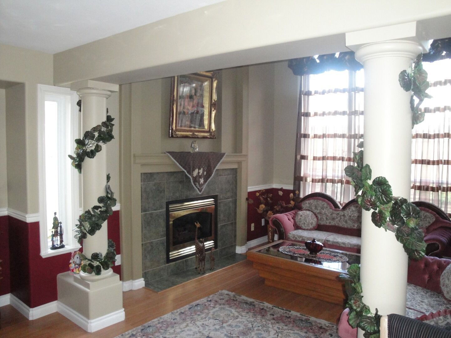 Living room with fireplace, cushioned chairs, and large windows with decorative plants.