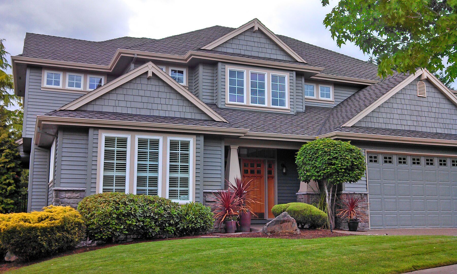 Suburban two-story gray house with red front door, manicured lawn, and two-car garage