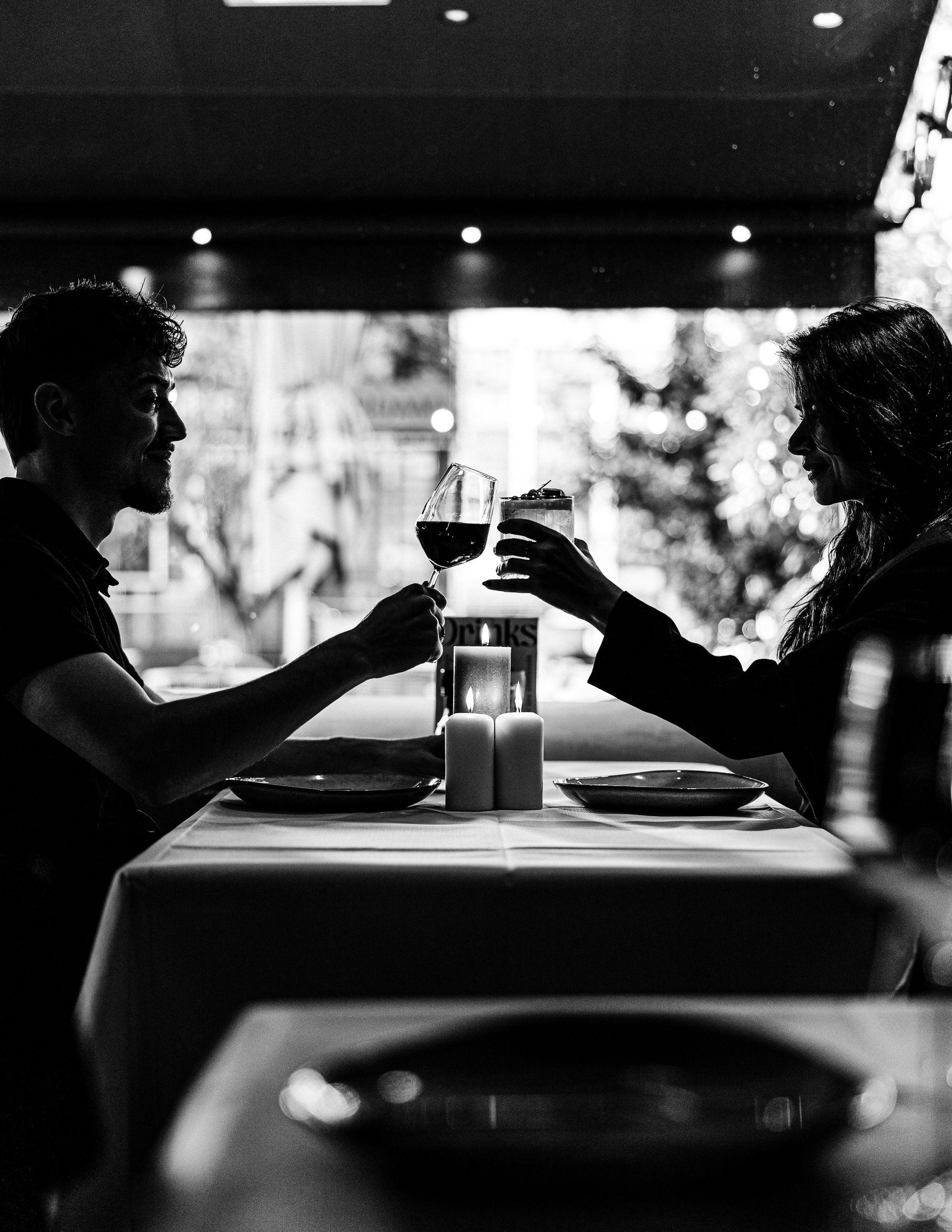 Person holding a large sandwich wrapped in paper, against a blurred outdoor background.