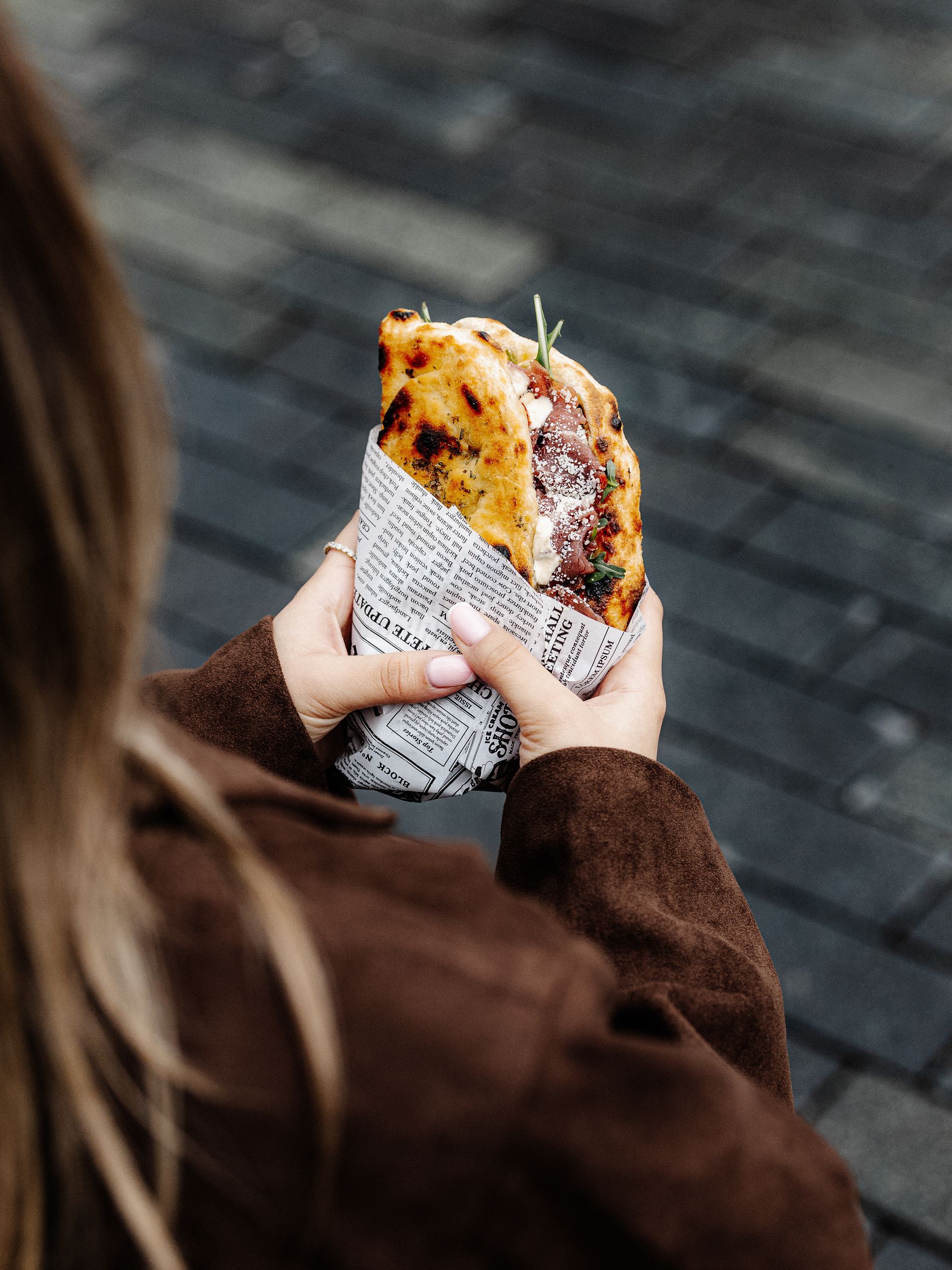 Person holding a large sandwich wrapped in paper, against a blurred outdoor background.