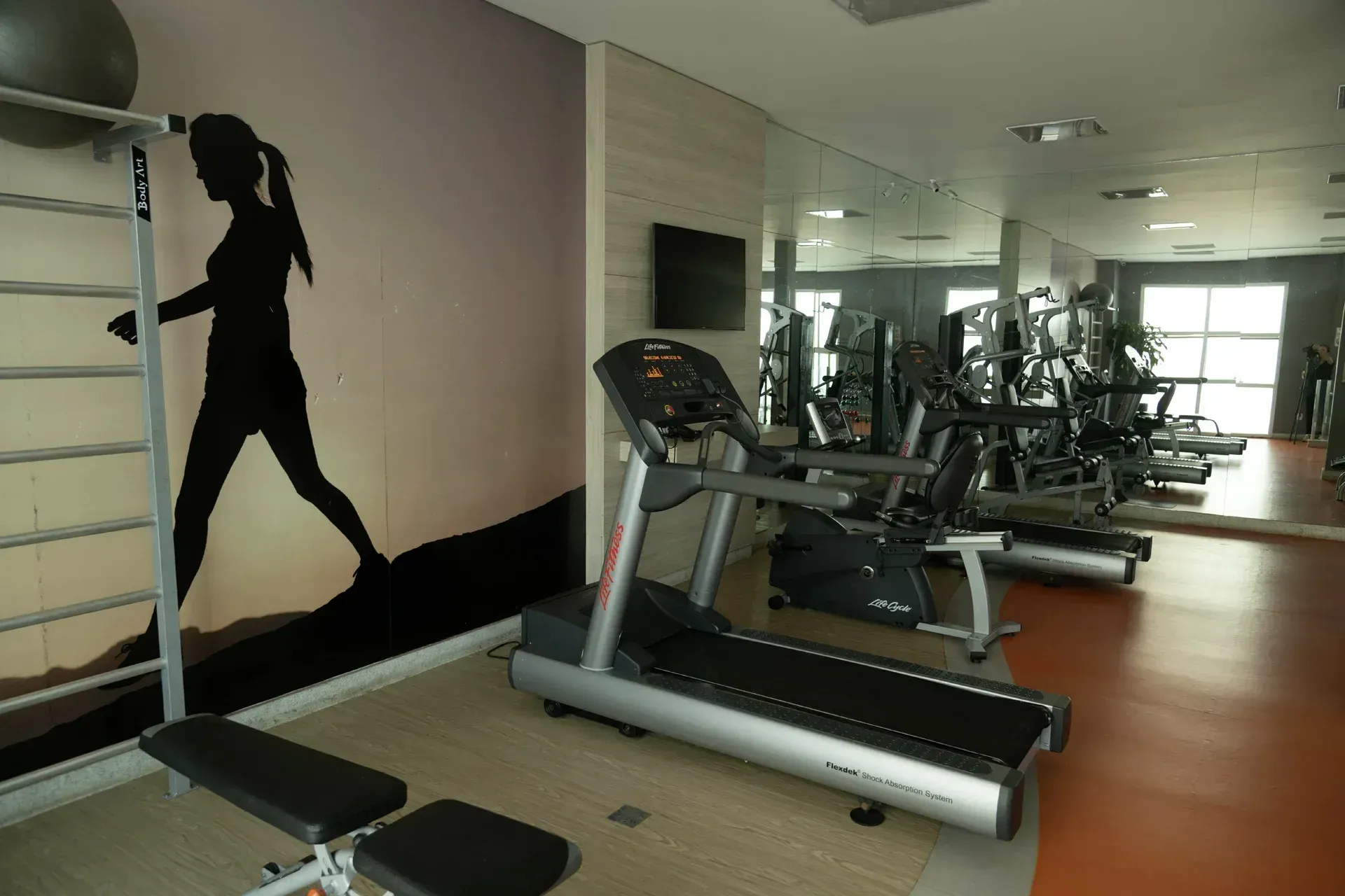 Uma academia com esteiras e uma foto de uma mulher na parede