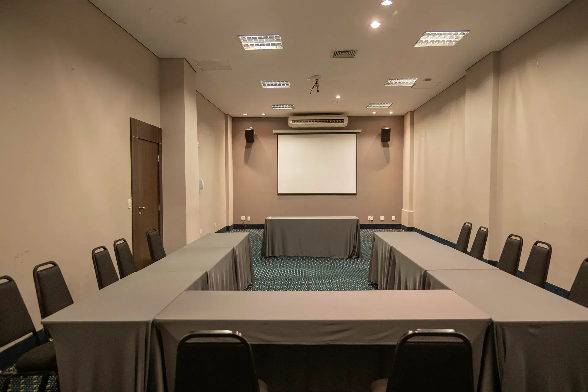 Uma sala de conferências com mesas e cadeiras e uma tela de projetor.