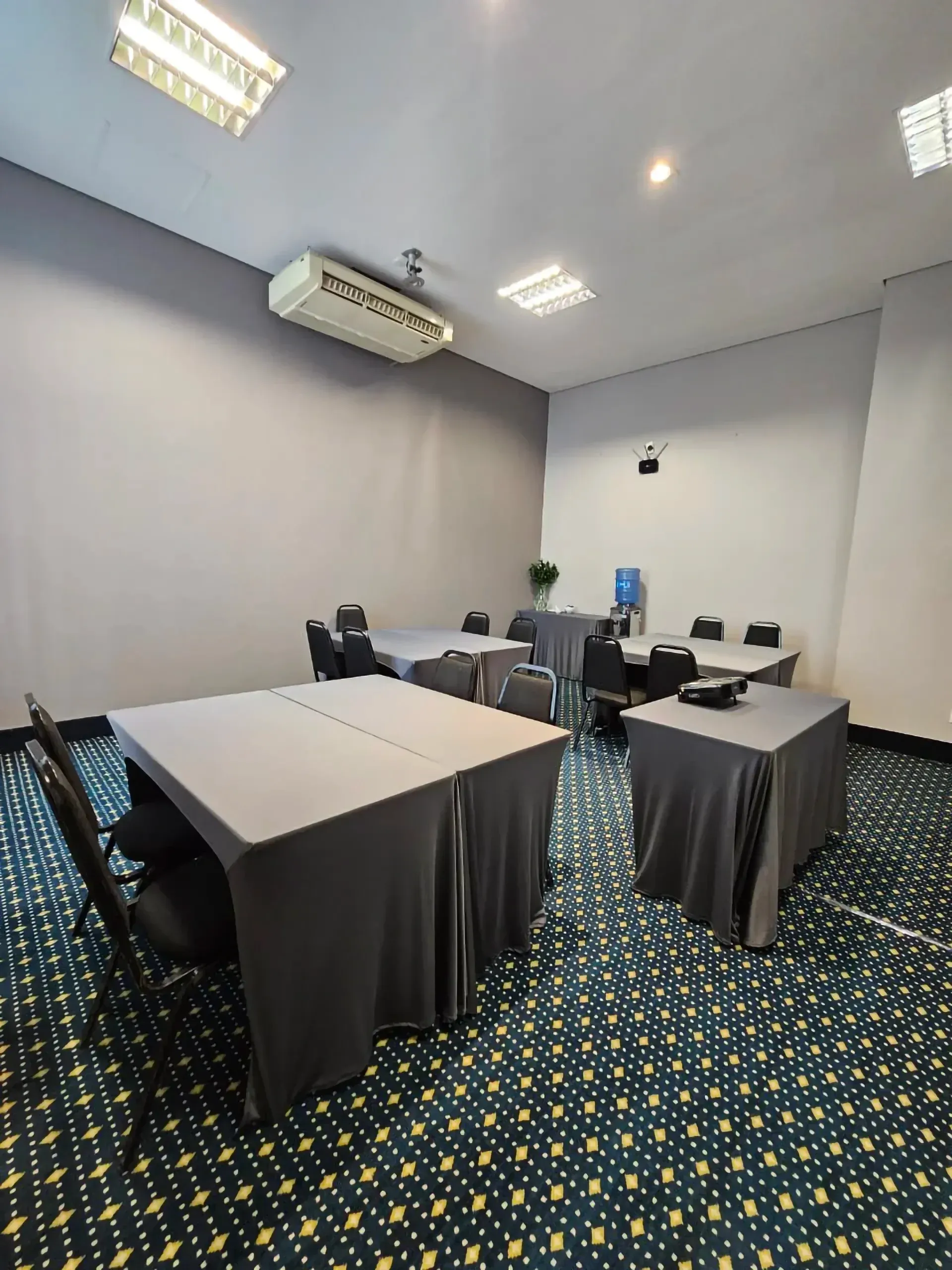 Uma sala de conferências com mesas e cadeiras e um projetor no teto.