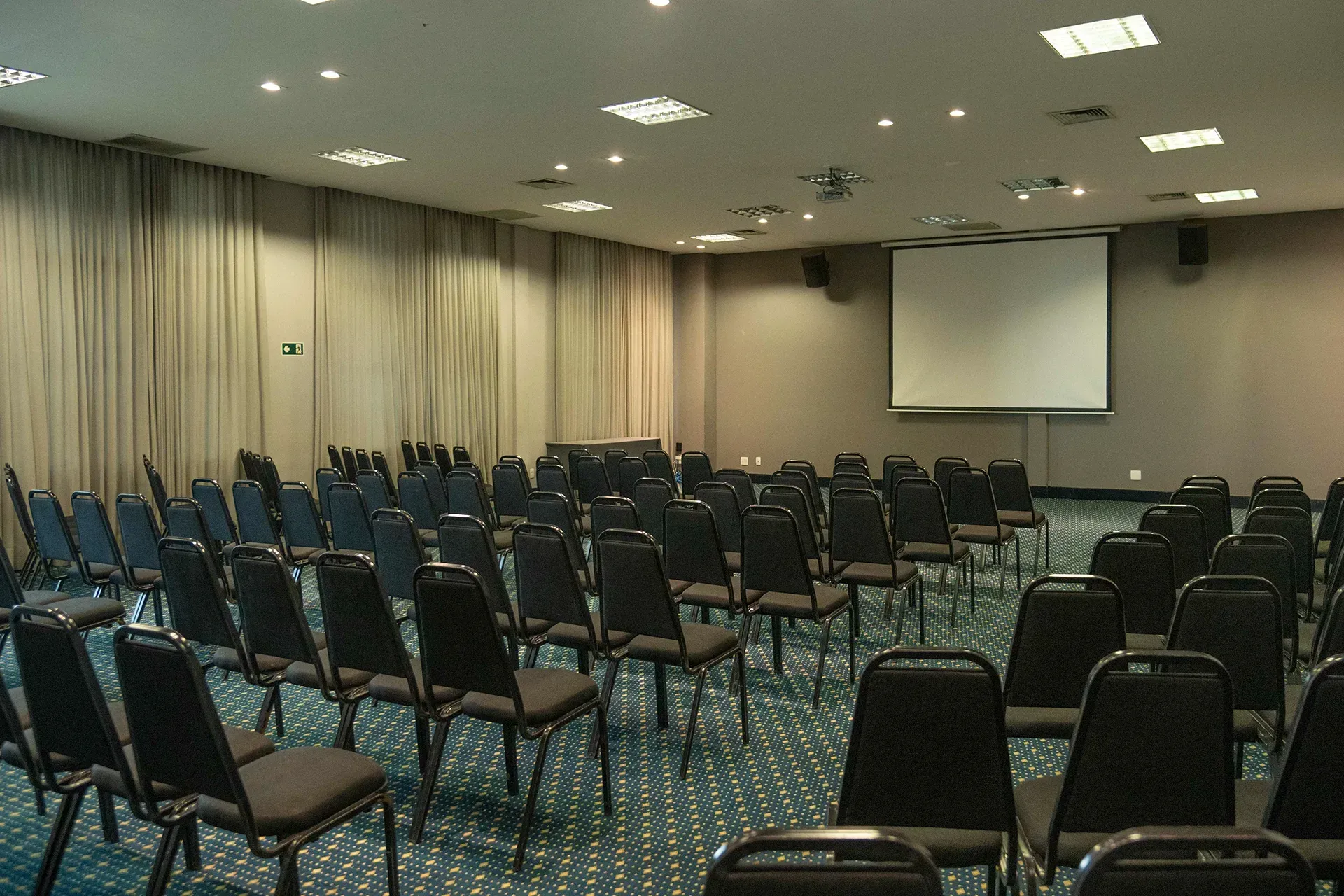 Uma sala de conferências com fileiras de cadeiras e uma tela de projetor