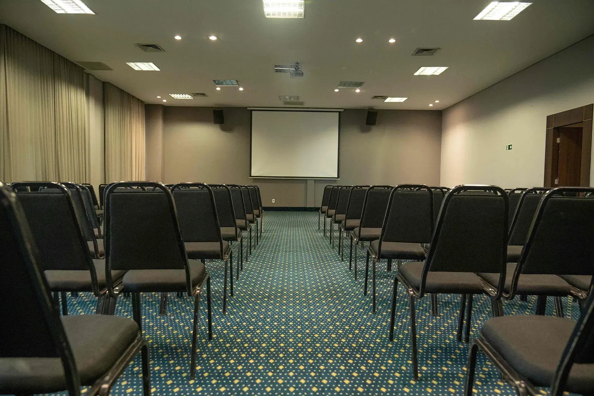 Uma sala de conferências vazia com fileiras de cadeiras e uma tela de projetor