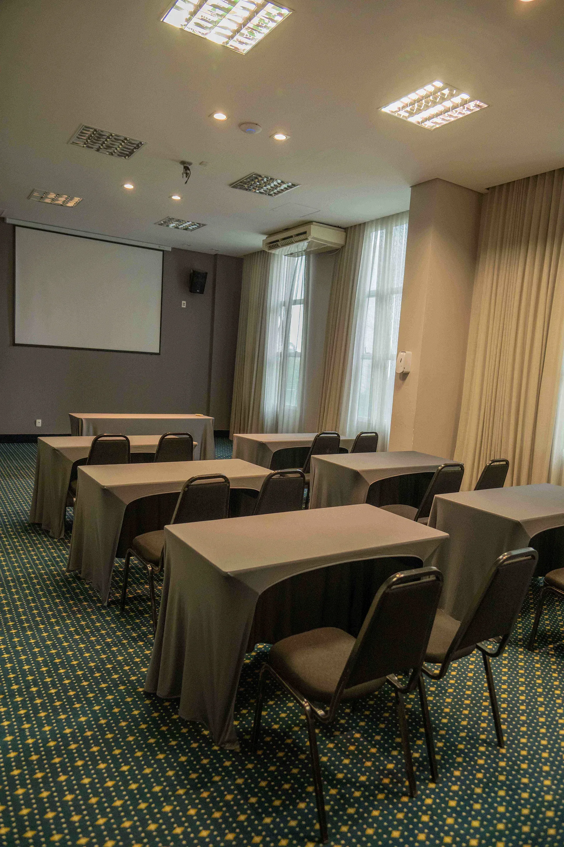 Uma sala de conferências com mesas e cadeiras e uma tela de projetor.