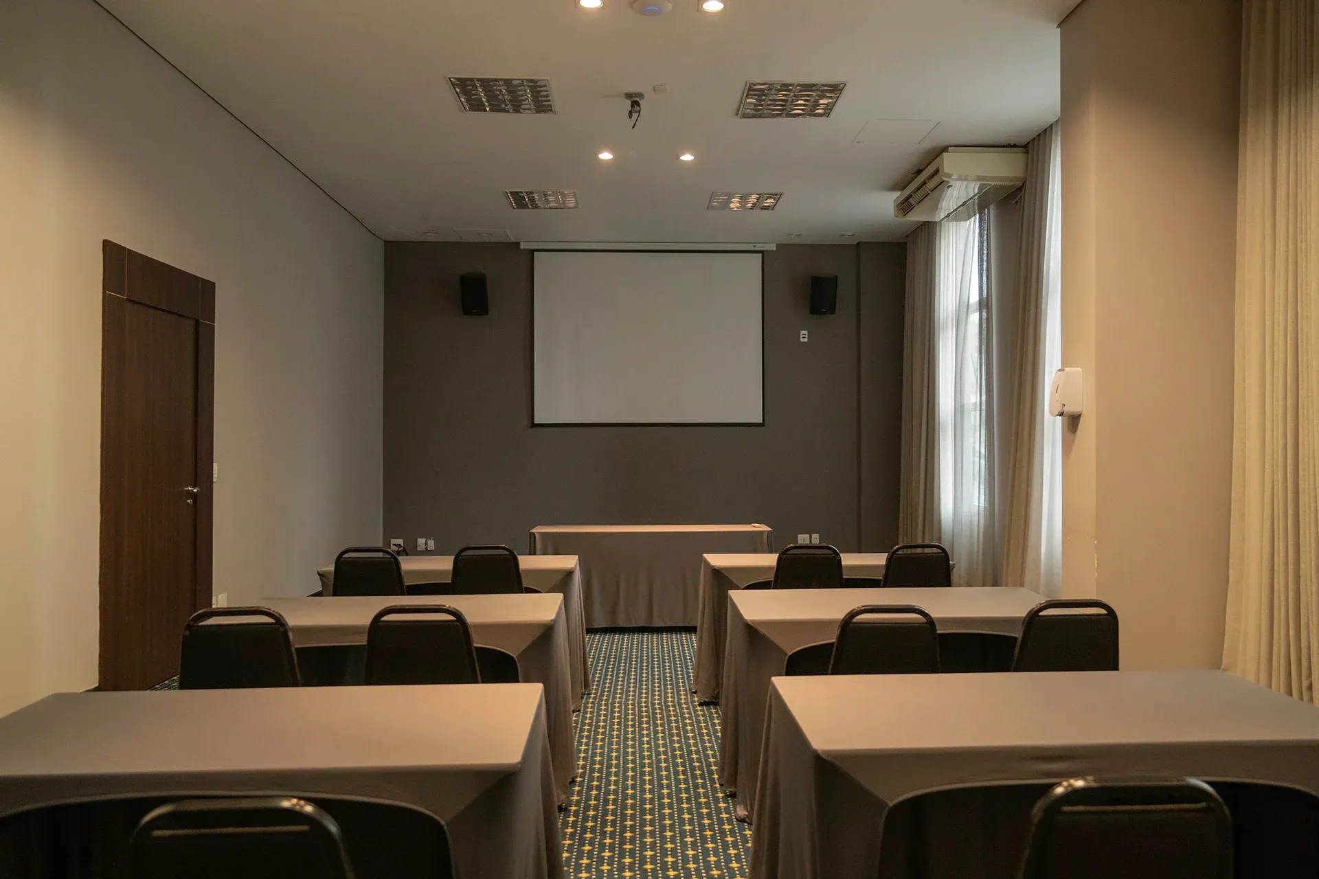 Uma sala de conferências com mesas e cadeiras e uma tela de projetor