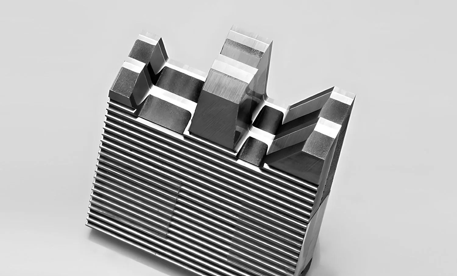 A close-up, grayscale view of a metal die with horizontal grooves and a stepped profile.