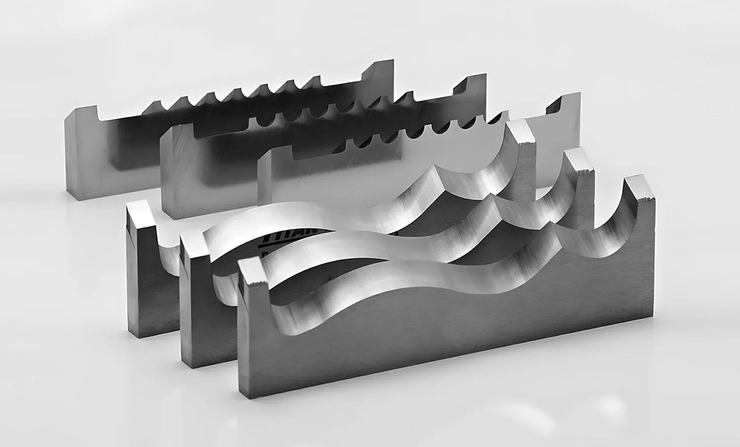 Three metal machine vise jaws with different textured gripping surfaces, arranged on a reflective surface.