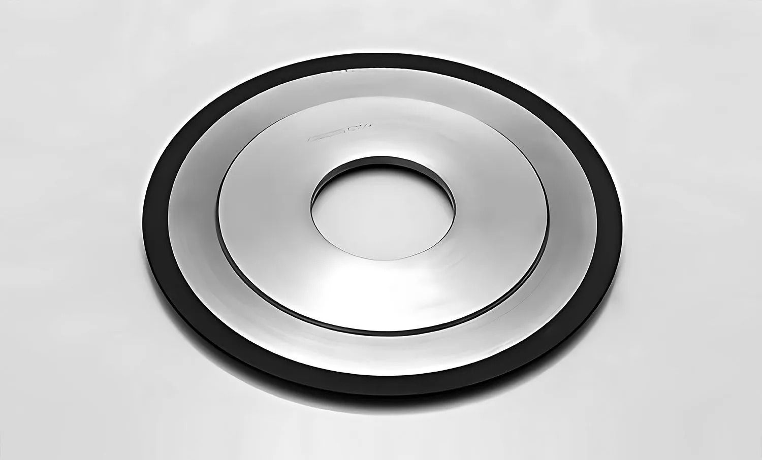 A layered, circular metallic component with a central hole and a black rubber edge.