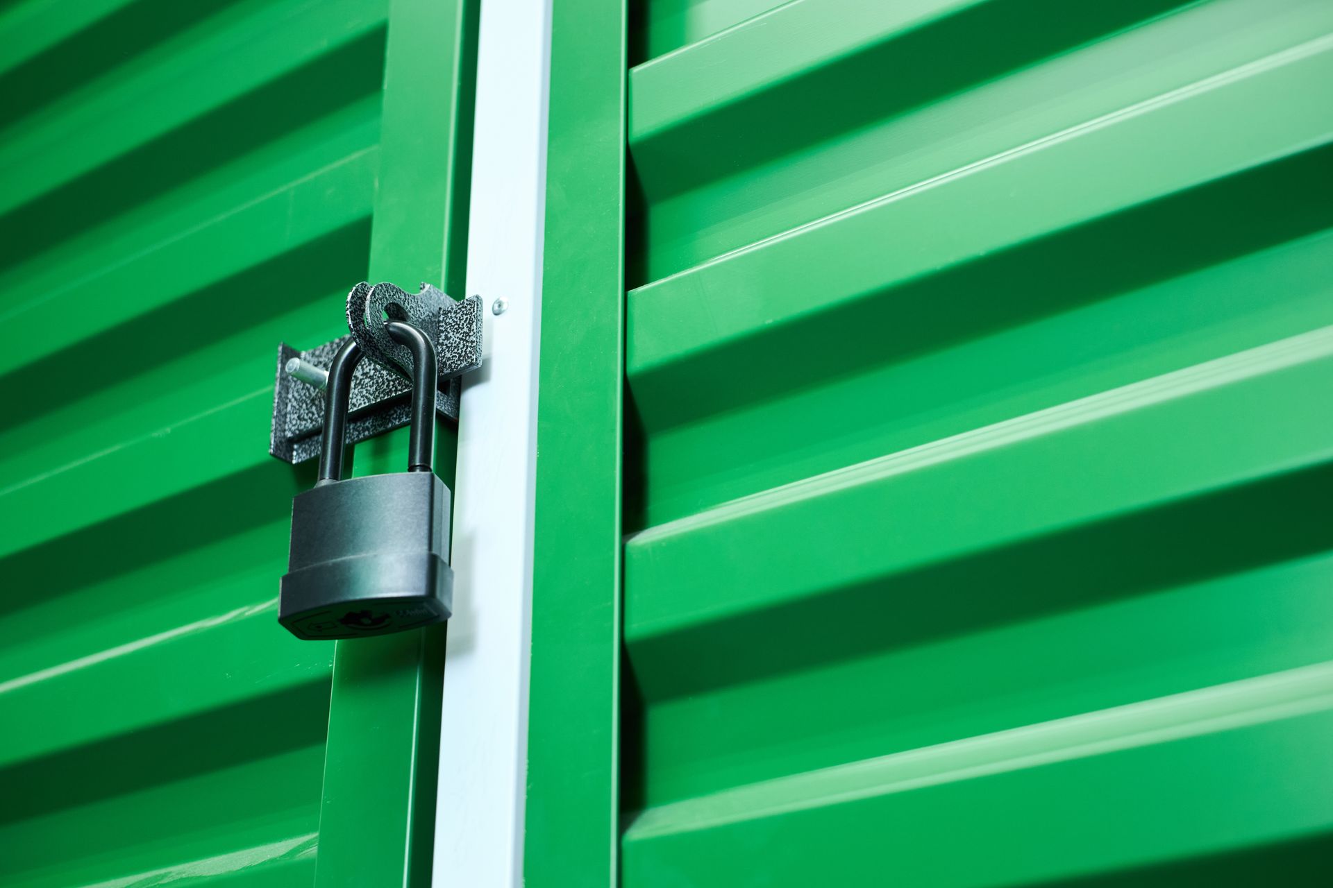 Closeup of metal padlock securing green corrugated metal storage unit door.