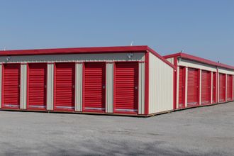 A row of mini storage and self storage units are under the sun, showcasing their red doors.