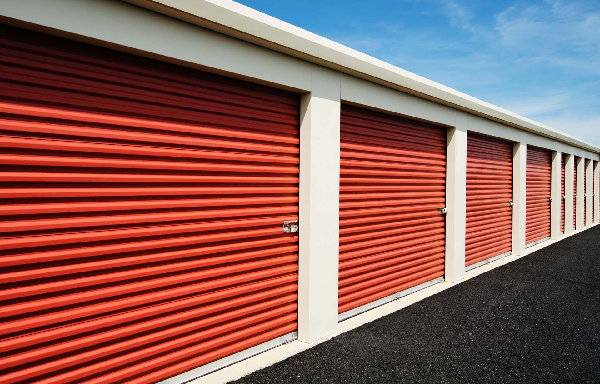 Row of red storage unit doors at outdoor self storage facility.
