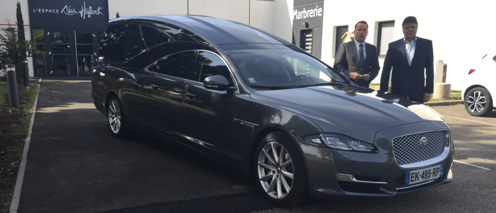Une voiture funéraire est garée devant un bâtiment.