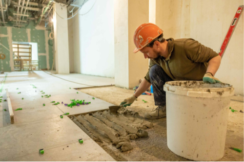 Un homme portant un casque de chantier pose des carreaux sur le sol.