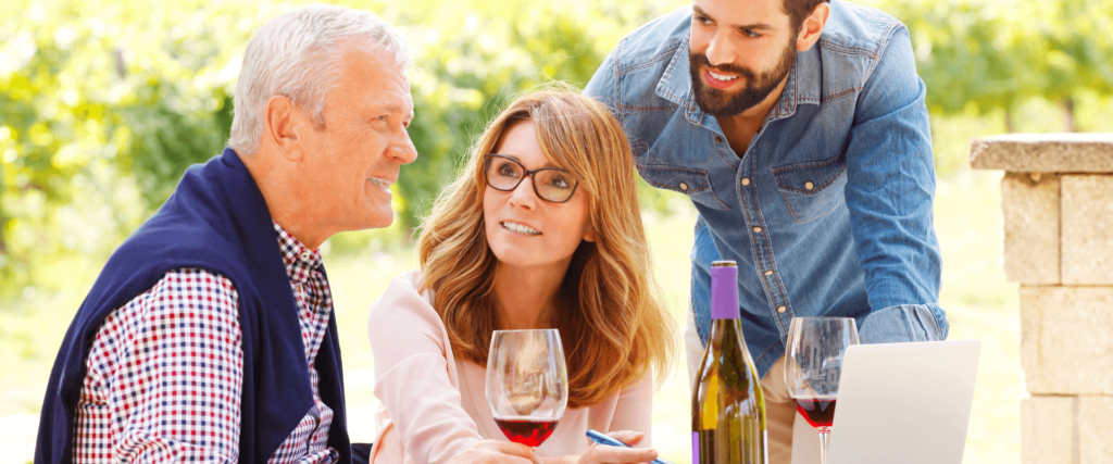 Un groupe de personnes est assis à une table avec des verres à vin et un ordinateur portable.
