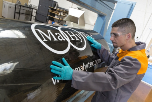 Un homme portant des gants bleus travaille sur un panneau indiquant mahytec.com