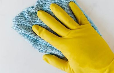 Une main dans un gant en caoutchouc jaune tient une serviette bleue.