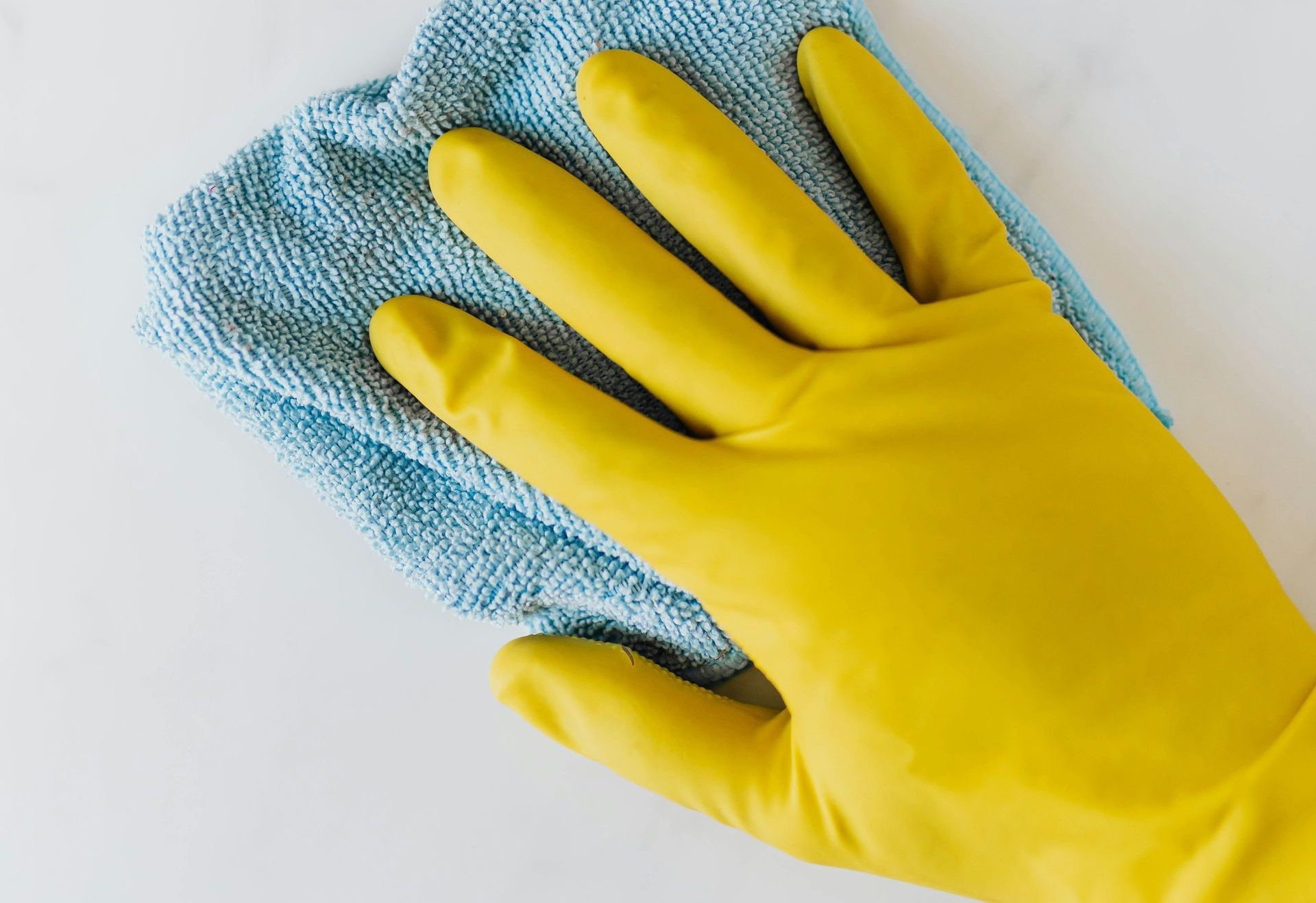 Une personne portant des gants en caoutchouc jaunes nettoie une surface blanche avec un chiffon bleu.