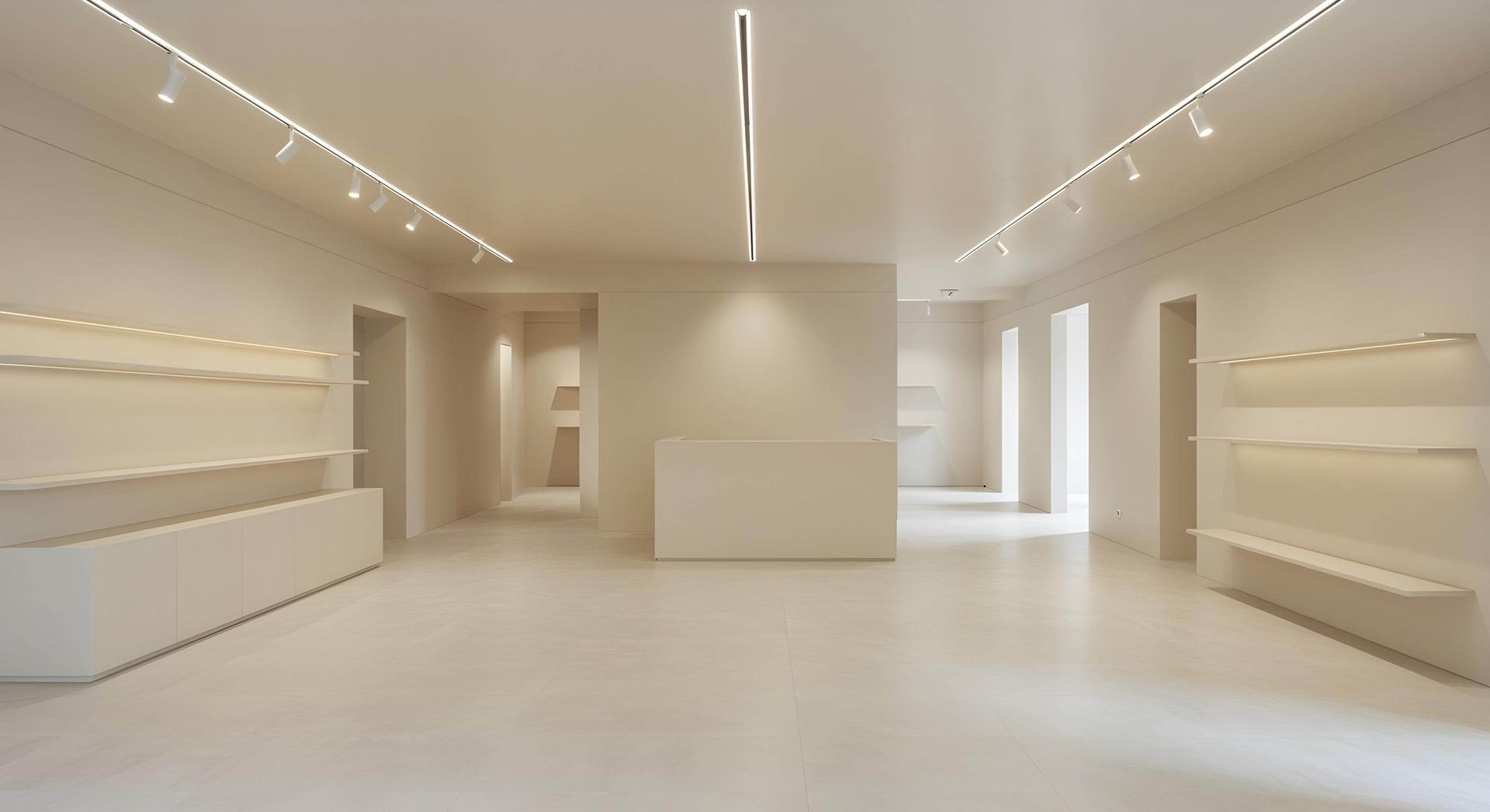 Espacio comercial vacío, minimalista, de color crema, con iluminación empotrada, estantes y puertas.