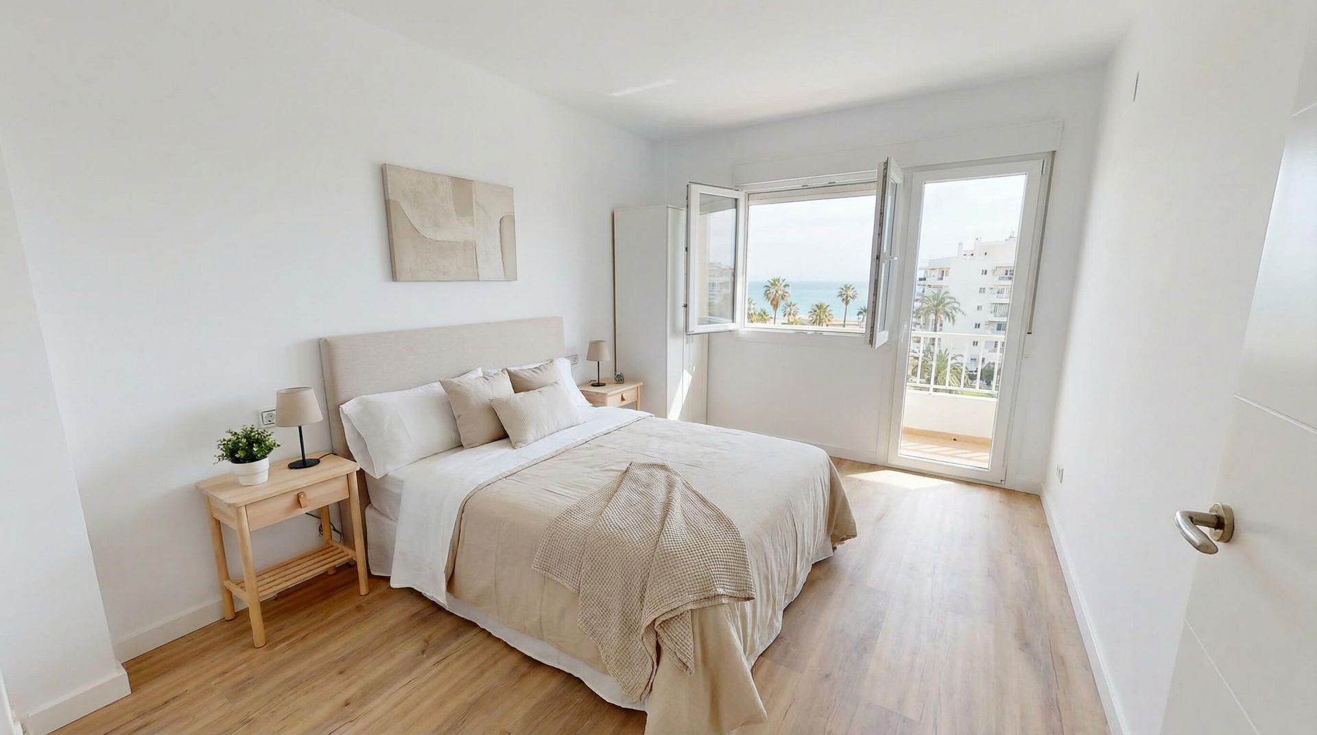 Dormitorio con cama, mesitas de noche y puerta a balcón con vista al mar.