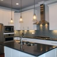 A modern kitchen with white cabinets, dark gray countertops, a large island, stainless steel appliances, and lighting.