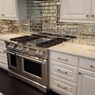 A stainless steel range stove in a white kitchen with mirrored, rectangular subway tile backsplash and white cabinets.