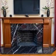 A wooden mantel fireplace featuring black and white marble tiling, topped with a flat-screen TV and two vases of flowers.