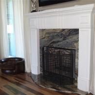 A white fireplace mantel with a dark, marbled stone surround, a black metal fire screen, and dark wood flooring.