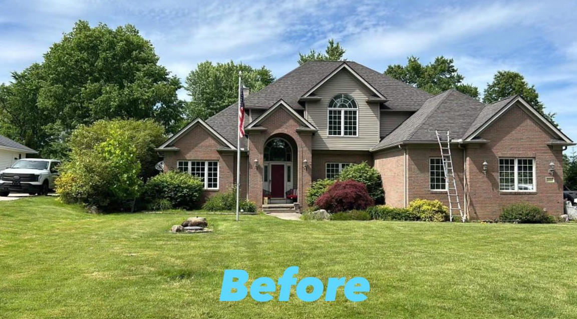 A large brick house with a gray roof is sitting on top of a lush green lawn.