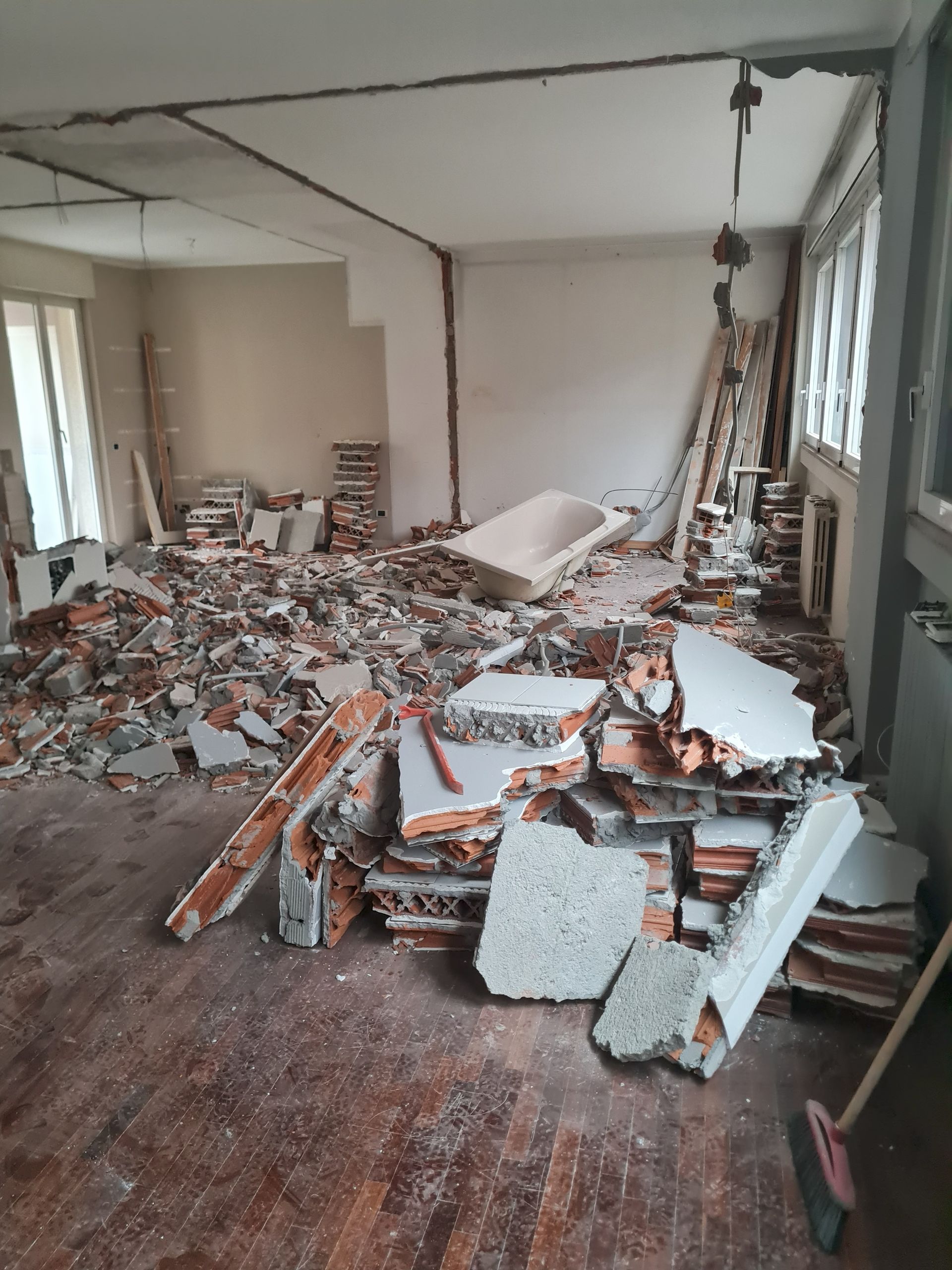 Demolizione di una stanza interna. Il cumulo di detriti copre il pavimento; pareti e finestre sono esposte.