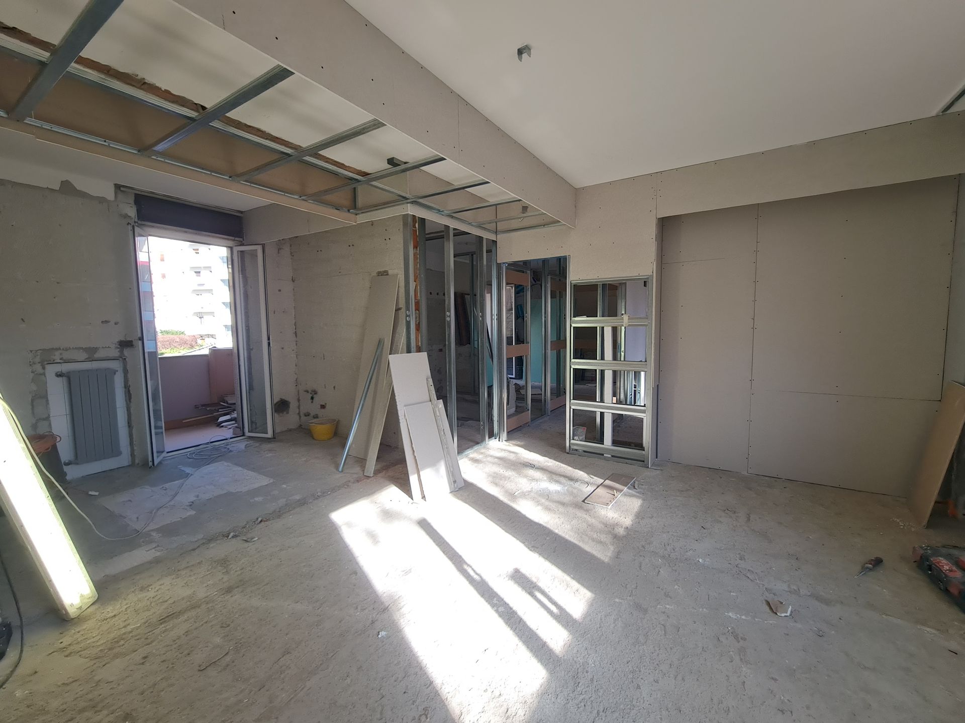 Interno in costruzione, con travi a vista, cartongesso e porta d'accesso al balcone.
