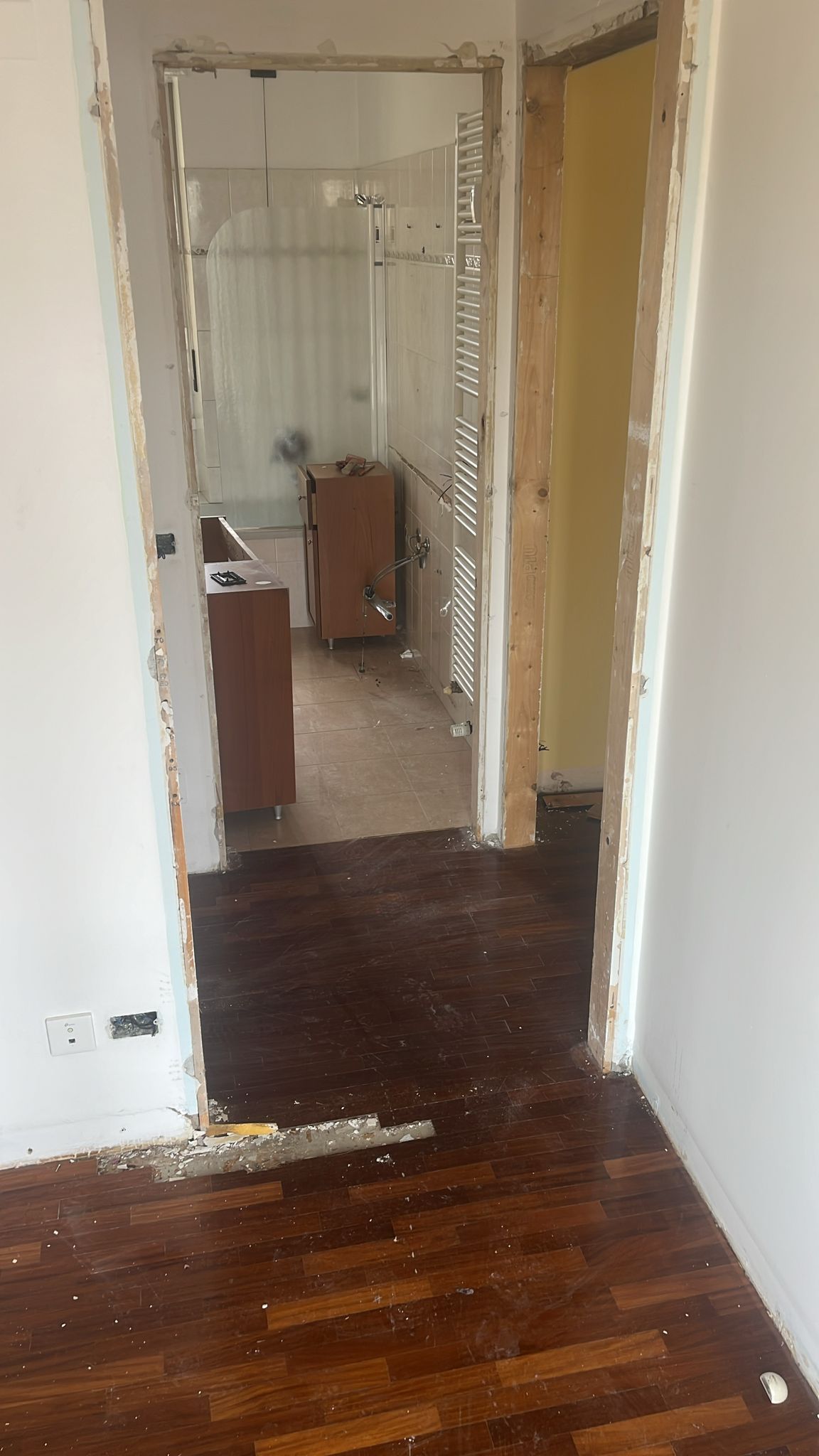 Porta che conduce a una stanza con pareti danneggiate e pavimento in legno scuro. È visibile un mobiletto.