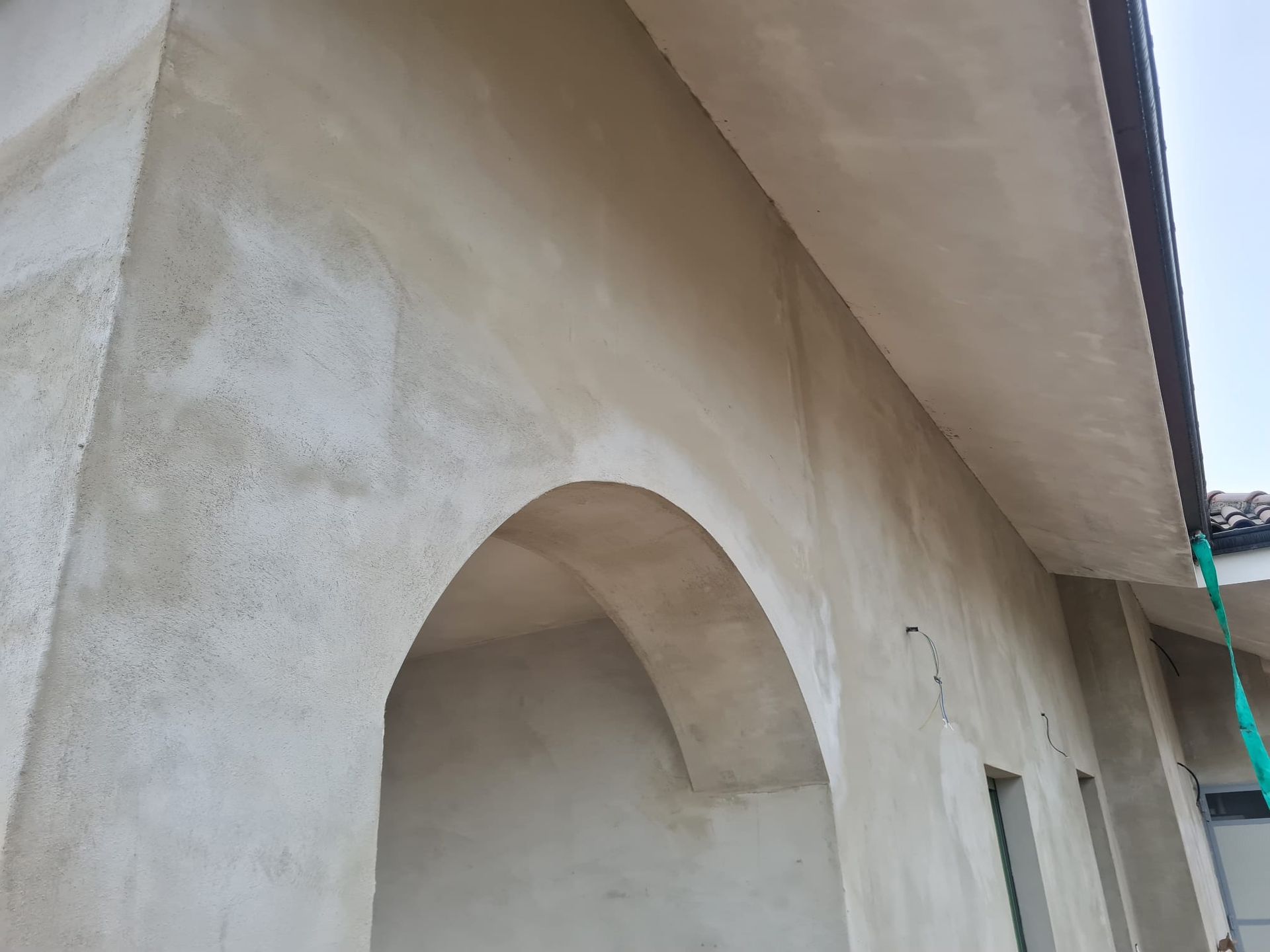 Esterno di un edificio con finitura in stucco beige chiaro, porta ad arco e tetto piano.
