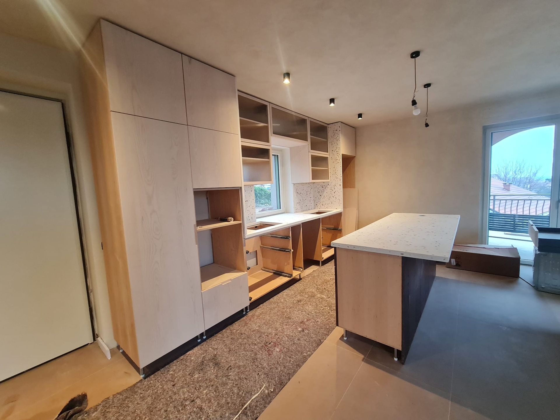 Mobili da cucina e isola in costruzione; ripiani aperti, tonalità legno chiaro, non rifiniti.