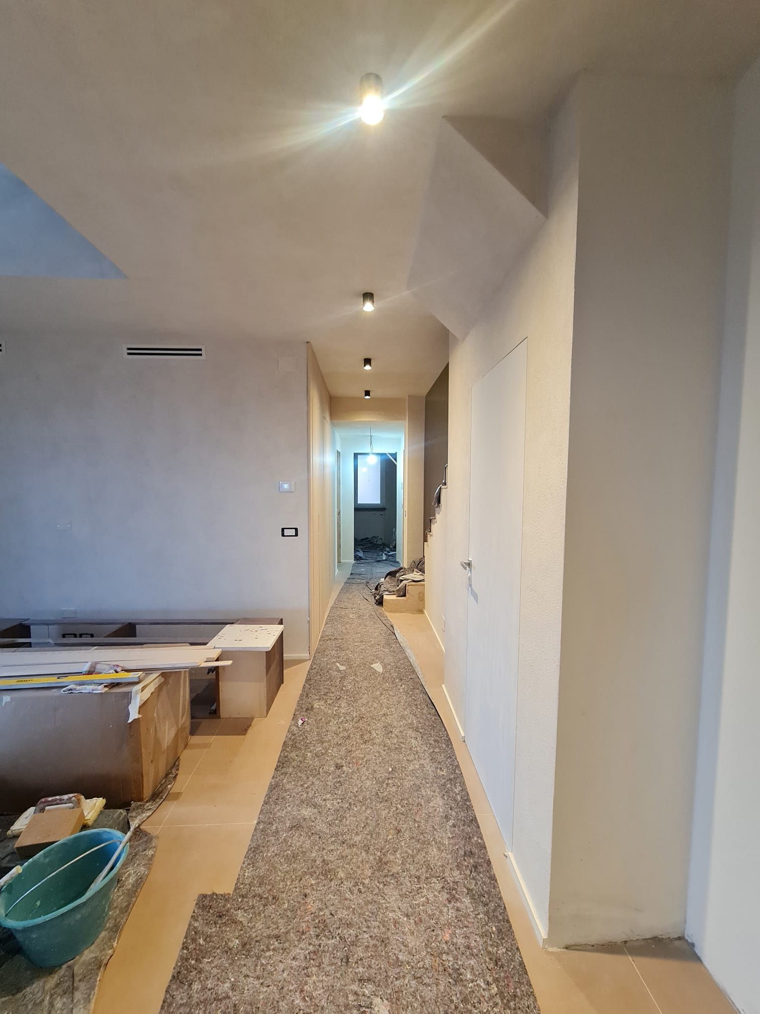 Corridoio in costruzione; apparecchi di illuminazione installati; pavimento in cemento in opera.