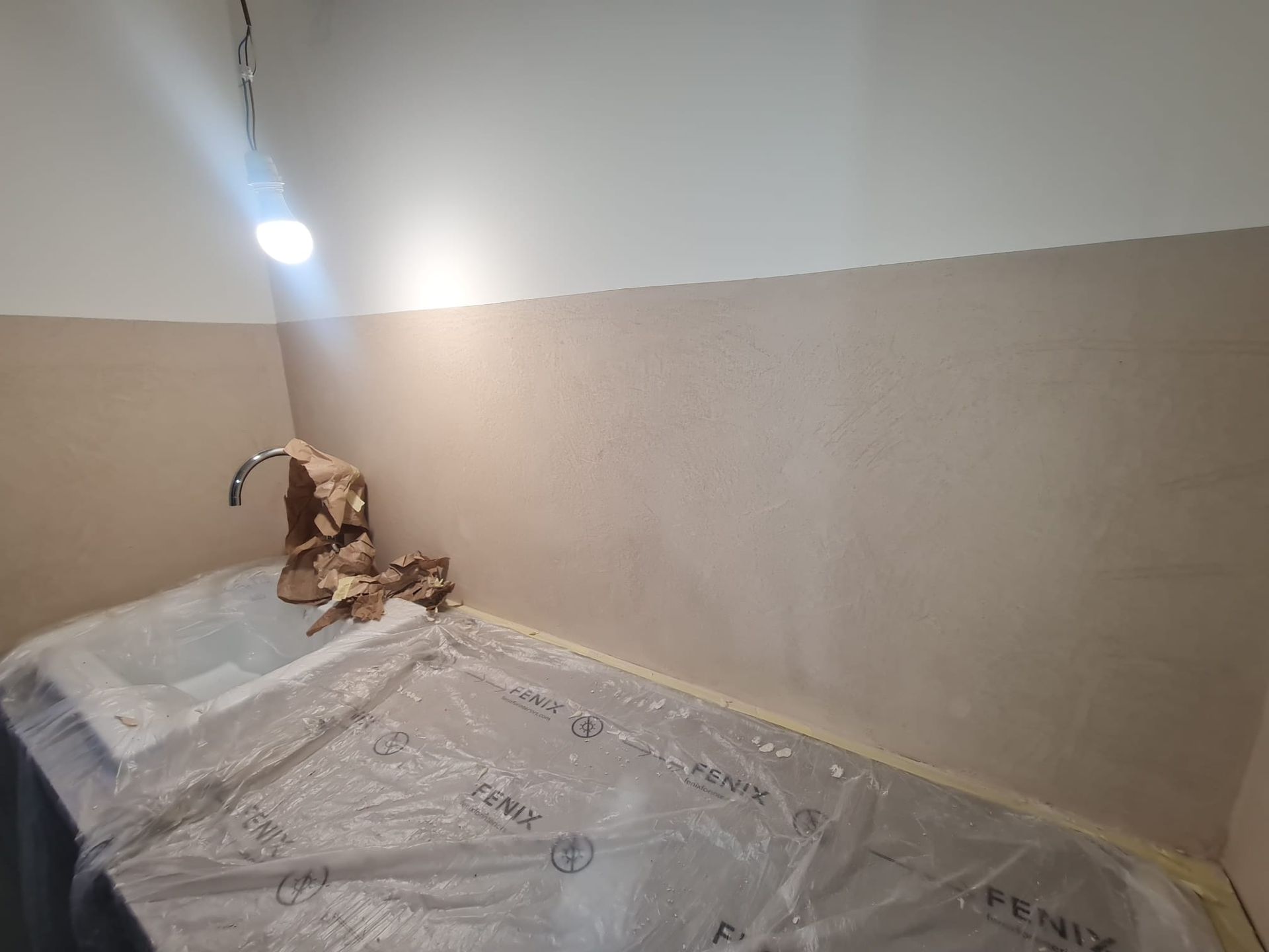 Bagno in costruzione con lavandino, rubinetto e piano. Pareti beige, soffitto bianco.