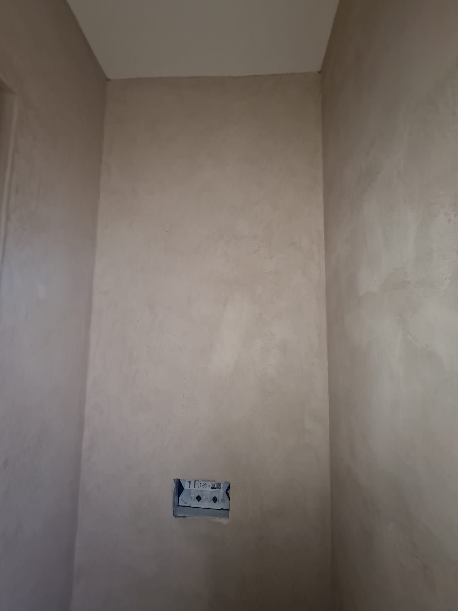 Angolo interno di una stanza con pareti di colore marrone chiaro e una presa elettrica.