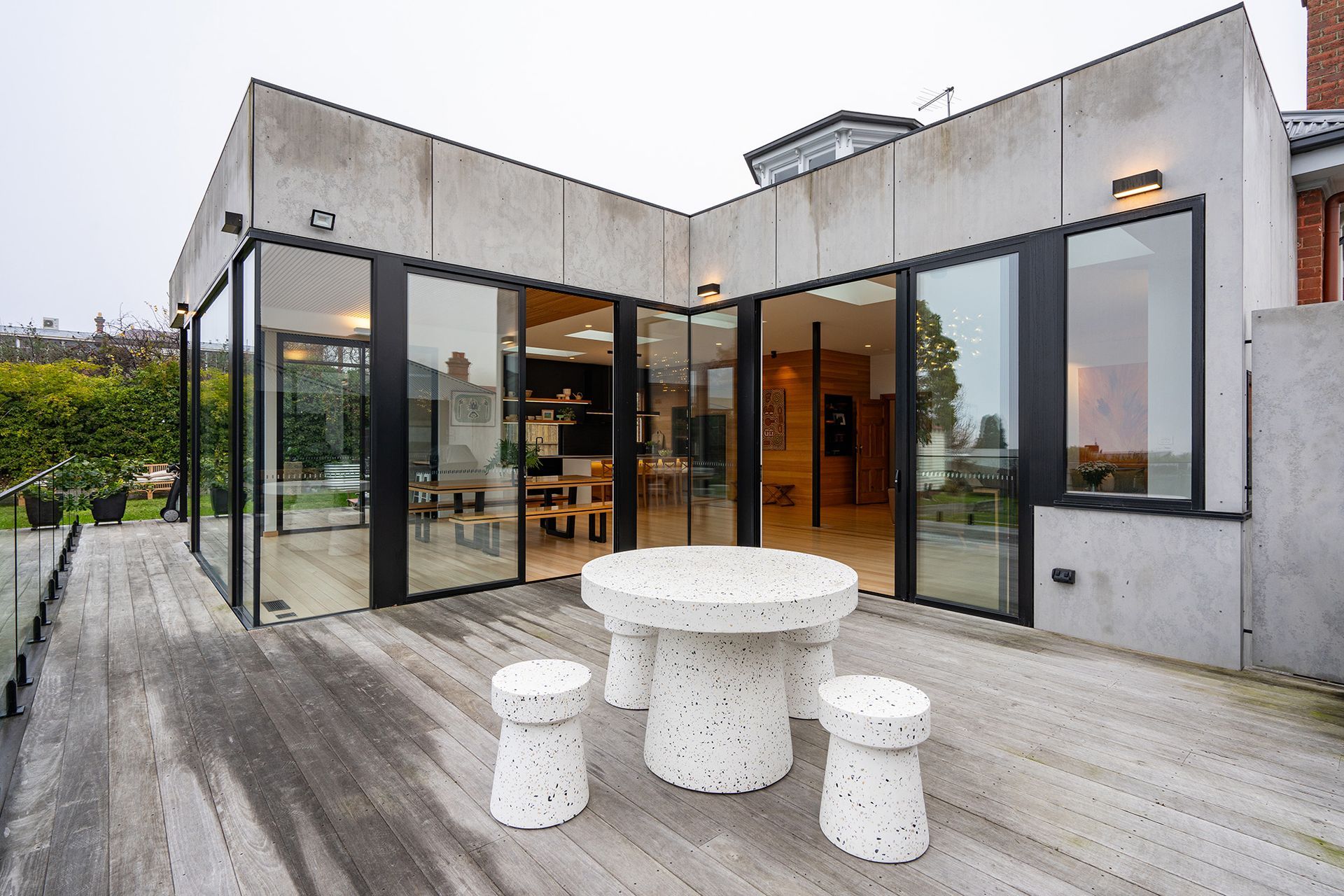 There is a table and stools on the deck of a house.