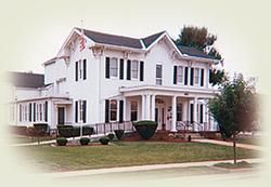 A large white house with a porch and trees in front of it.