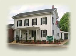 A large white house with black shutters and a sign in front of it.