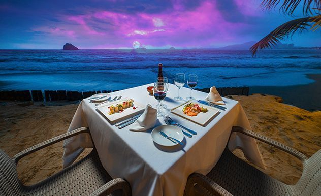Cena romántica junto al mar al atardecer con vistas al océano y cielo púrpura.