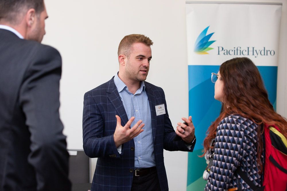 A man in a suit is talking to a woman in front of a pacific hydro sign.
