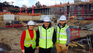 Three construction workers are posing for a picture at a construction site.